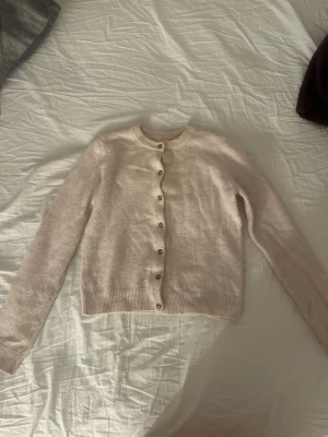 Ljusrosa kofta från H&M XS - Supersöt ljusrosa kofta från H&M i storlek XS. Koftan har rund halsringning, ribbade muddar och knappar framtill. Perfekt att slänga över en topp eller bära stängd för en clean look.