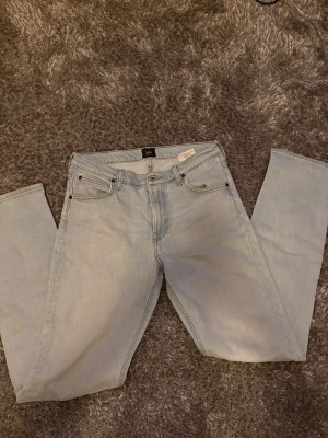 Ljusblå Lee jeans W31 L34 - Säljer ett par ljusblå jeans från Lee i modellen WEST, tillverkade i ekologisk bomull. Klassisk femficksdesign, raka ben och snyggt Lee-läderpatch bak. Perfekta för dig som gillar vintagevibbar och relaxed fit.