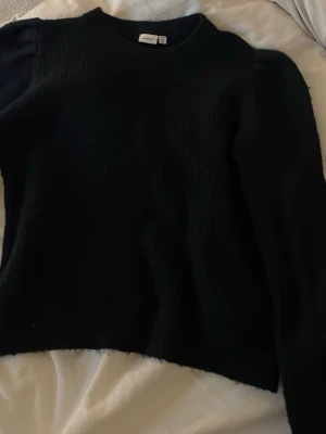 Svart stickad tröja från Monki - En enkel svart stickad tröja från name it med rund hals och långa ärmar. Tröjan har en klassisk passform och är perfekt att matcha med jeans eller kjol. Materialet känns mjukt och passar bra till kyligare dagar.