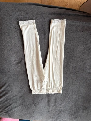 Vit spetsdetaljerad väst från Lindex - Säljer en vit väst från Lindex med elastisk nederkant och fina spetsdetaljer upptill. Västen är gjord i mjukt material och har en enkel, rak passform. Perfekt för att addera en söt touch till din outfit.