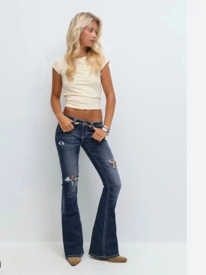 Mörkblå bootcut jeans med slitningar - Snygga mörkblå jeans med bootcut-modell och slitna detaljer på benen. Jeansen har låg midja, kontrastsömmar och broderade bakfickor. Perfekta för dig som gillar en avslappnad och trendig look.