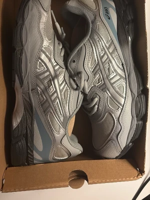 Grå sneakers från Asics - Säljer ett par grå sneakers från Asics med coola detaljer i mesh och syntet. Skorna har snörning och en chunky sula som ger en sportig vibe. Perfekta för dig som gillar stilrena och bekväma skor till vardags eller träning. Helt nya!!