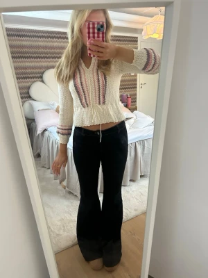 Randig stickad kofta med snörning - Superfin stickad kofta i vitt med randiga detaljer i rosa, lila och grått. Modellen är croppad med snörning i midjan och har långärmade ärmar. Perfekt för dig som gillar en söt och trendig look.