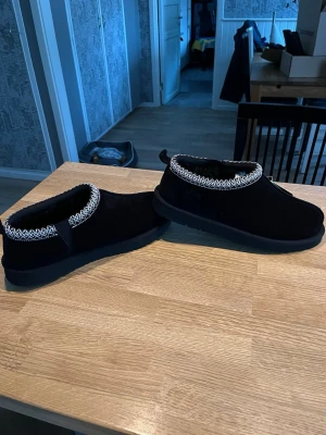 Svarta UGG Australian Shepherd boots - Svarta boots från UGG Tasman men med lite högre kant. Snyggt mönstrad kant i vitt och svart. Skorna har en rund tå, platt sula med grepp och är tillverkade i mocka. Perfekta för kalla dagar och har en stilren look som funkar till många outfits. Skorna är aldrig använda finns tyvärr ingen låda då jag köpte dem i Australien, fanns tyvärr då ingen plats i resväskan att få med sig dem 