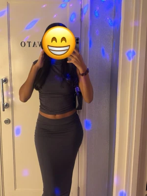 Mörk tight topp och kjol - Säljer en mörk, tight matchade topp och kjol med hög hals och ärmlös design. Klänningen har en enkel och stilren look som framhäver figuren. Perfekt för dig som gillar minimalistisk stil och vill ha något som känns både trendigt och bekvämt.