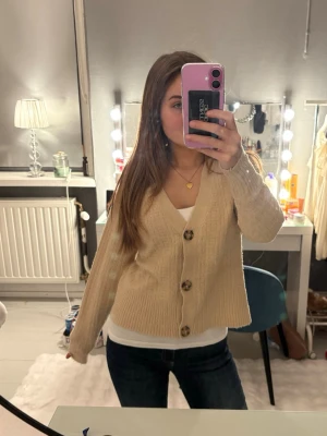 Beige kofta från 157 med stora knappar - Supermysig beige kofta från 157 i stickat material. Koftan har v-ringning, stora mönstrade knappar och ribbade muddar. Perfekt att slänga på sig över ett linne eller t-shirt. Snyggt rutmönster i stickningen och avslappnad passform ❣️