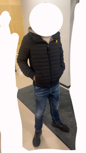 Svart dunjacka från Parajumpers - Säljer en svart dunjacka från Parajumpers med coolt badge på bröstet och orange detalj vid kragen. Jackan är quiltad och har dragkedja samt fickor med zip. Insidan är silverfärgad och materialet är lätt och syntetiskt. Perfekt för kalla dagar och riktigt snygg stil.