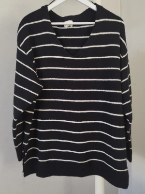 Svartvit randig tröja - Mysig svart stickad tröja med vita horisontella ränder och v-ringad hals. Tröjan har lång ärm och slits i sidorna nedtill för en avslappnad look. Perfekt för kyliga dagar och enkel att matcha med jeans eller kjol.