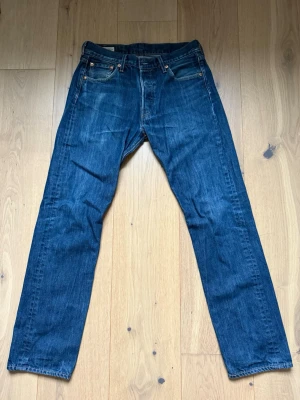 Levi's 501 blå jeans W30 L32 - Klassiska Levi's 501 jeans i mörkblå färg med raka ben och fem fickor. Perfekta för dig som gillar tidlös denimstil. W30 L32 Ny pris 1299KR Priset kan diskuteras vid snabb affär.