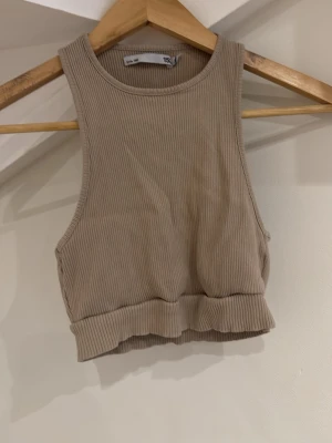 Beige ribbad croppad linnetopp - Säljer en beige croppad linnetopp från Lager 157i xs/s. Toppen är ribbad och har breda axelband samt rund halsringning. Perfekt till sommaren och enkel att matcha med jeans eller kjol.
