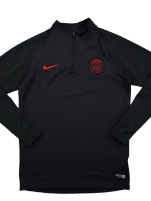 Svart Nike PSG träningströja - Säljer en svart långärmad träningströja från Nike med PSG-logga och röd Nike swoosh på bröstet. Tröjan har half zip och är tillverkad i ett lätt, syntetiskt material som passar perfekt för fotbollsträning.