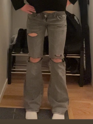 Grå bootcut jeans från Gina Tricot - Säljer ett par gråa bootcut jeans från Gina Tricot i storlek 152. Jeansen har slitna detaljer med stora hål som jag har klippt själv. 