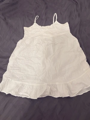 Vit sommarklänning från Gina Tricot - Supersöt vit kort klänning från Gina Tricot med tunna axelband och volangkant nertill. Perfekt för varma dagar och har en luftig passform som känns riktigt chill. Tillverkad i ett lätt material som känns skönt mot huden. Använd tre gånger så ganska bra o ny skick.