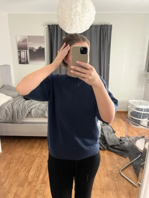 Mörkblå stickad tröja med halvärm - Mysig mörkblå stickad tröja med rund halsringning och halvärmar. Tröjan har en enkel och stilren design, perfekt att slänga på sig när det är lite kyligare ute. Passformen är lite loose och materialet känns mjukt mot huden.storlek 170! Aldrig använd