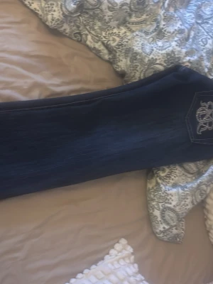 Mörkblå jeans med strassdetaljer - Snygga mörkblå jeans med lite utsvängda ben och coola strassdetaljer längs fickor och bakficka. Jeansen har ett broderat mönster i strass på bakfickan som ger extra bling. Materialet är klassisk jeans och passformen är normal med midwaist.