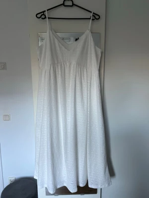 Vit klänning från Vero Moda - Säljer en vit klänning från Vero Moda i storlek XL. Klänningen har smala axelband med, v-ringad hals och ett broderat hålmönster över hela tyget. Axelbanden är insydda lite, se bild.