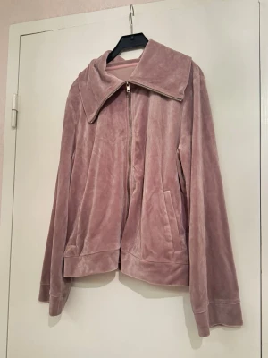Rosa velour hoodie med dragkedja - Mjuk och skön hoodie i ljusrosa velour med bred krage och hel dragkedja framtill. Tröjan har långa ärmar och två fickor på sidorna. Perfekt för chill dagar och har en loose passform som ger en avslappnad vibe. Du kan ha på dig den hemma eller under en jacka 😊 Jag har på mig S/M så den satt som en baggy jacka. Endast använd ett par gånger. Fått den som present så vet inte vart den är köpt från. 