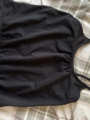 Svart träningstopp från FP Movement - Säljer en svart träningstopp från FP Movement i storlek S. Toppen har ett snyggt mönster i tyget och smala axelband som korsas i ryggen. Materialet är mjukt och stretchigt, perfekt för aktiva dagar. Passformen är tight och toppen är ärmlös med inbyggd bh. 