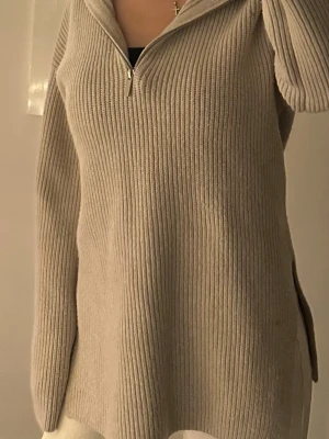 Beige ribbad stickad tröja med half zip - Säljer en beige stickad tröja med ribbad struktur och hög krage. Tröjan har en half zip-dragkedja framtill och långa ärmar. Inköp H&M