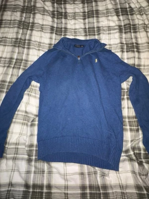 Blå stickad tröja Polo Ralph Lauren - Säljer en blå stickad tröja från Polo Ralph Lauren i storlek L. Tröjan har half zip med läderdetalj, ribbade muddar och krage. Klassisk gul logga broderad på bröstet. Perfekt för dig som gillar stilrena och bekväma plagg.