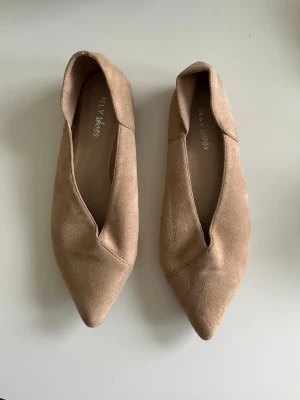 Beige ballerinaskor från NLY Shoes - Snygga ballerinaskor i beige syntetmocka från NLY Shoes med spetsig tå och låg profil. Skorna har en stilren design med djup v-ringad öppning framtill och platt sula. Perfekta för dig som gillar minimalistisk och trendig stil.