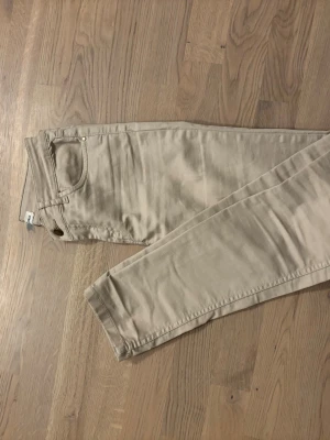 Beige chinos från Hampton Republic - Snygga beige chinos från Hampton Republic i storlek 34. Klassisk femficksmodell med knapp och dragkedja framtill. Byxorna har en rak passform och är tillverkade i mjuk bomull som känns skön mot huden. Perfekt för dig som gillar stilrena och enkla byxor.