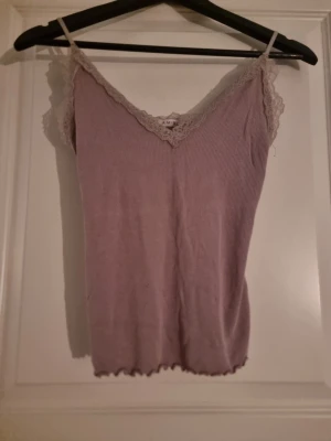 Ljuslila ribbad linnetopp med spets - Supersöt ljuslila ribbad linnetopp från AIM'N med tunna axelband och v-ringning. Toppen har fina spetsdetaljer längs urringningen och runt ärmhålen. Perfekt att styla med jeans eller kjol för en chill look.