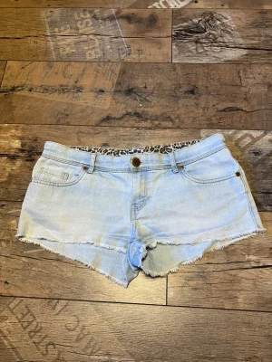 Lågmidjade ljusa shorts - Säljer ett par ljusblå jeansshorts från Denim Co. i storlek 38. Shortsen har råa, fransiga kanter och klassisk femficksdesign. Insidan av midjan har ett leopardmönstrat tyg som ger en cool detalj. Perfekta för varma dagar och chill stil.