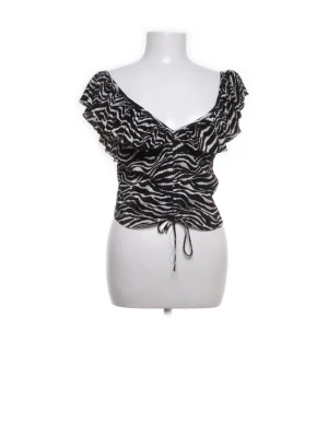 Zebramönstrad croppad blus med snörning - Säljer en svartvit zebramönstrad blus med volangdetaljer vid axlarna och v-ringad hals. Toppen är croppad och har snörning framtill för att justera passformen. Perfekt för dig som gillar djurmönster och vill sticka ut.