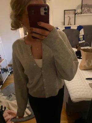 Ljusgrå kofta med knappar - Supermjuk ljusgrå kofta med rund hals och knäppning framtill. Långärmad och i en klassisk, lite loose passform. Perfekt att slänga över ett linne eller t-shirt. Enkel och stilren design som funkar till allt.