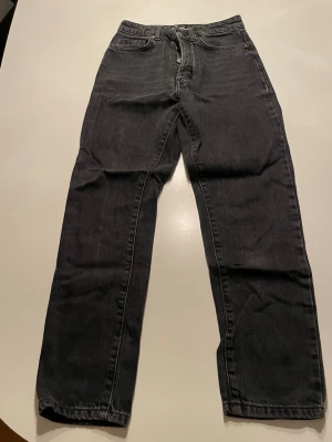 Svarta jeans från Never Denim, storlek 25 - Säljer ett par svarta jeans från Never Denim i rak modell. Jeansen har klassisk femficksdesign, knapp och dragkedja fram samt bälteshällor. Materialet är jeans och färgen är mörk svart. Perfekt för dig som gillar stilrena och enkla jeans.