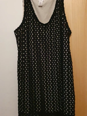 Klänning - Säljer en svart klänning från Motherhood i storlek L. Klänningen är ärmlös och har ett stickat, hålmönstrat tyg med vit underklänning. Den har en vit snörning i midjan som ger en snygg detalj. Perfekt för dig som gillar unik stil och vill ha något bekvämt.