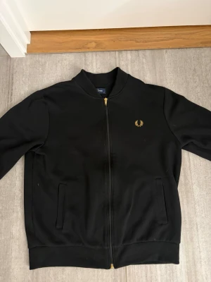 Svart ziptröja från Fred Perry - Svart ziptröja från Fred Perry med guldfärgad dragkedja och logga broderad på bröstet. Väldigt bra skick/ som ny använd ett fåtal gånger. Säljer även denna då den blivit för liten.