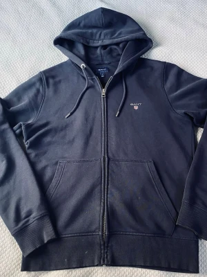 Gant zip hoodie - Säljer en gant zip hoodie i storlek M. Tjocktröjan har inga hål eller defekter förutom att det finns lite vit färg som knappt syns längst nere (se bild). Har du frågor så krig gärna till mig :)