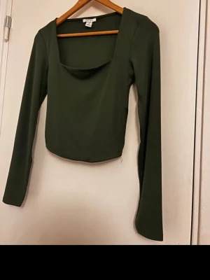 Mörkgrön croppad topp från Amisu - Snygg mörkgrön croppad topp från Amisu med lång ärm och fyrkantig halsringning. Toppens material är mjukt och stretchigt, vilket gör den bekväm att bära. Passformen är slim och den har en stilren, enkel design utan mönster eller extra detaljer.