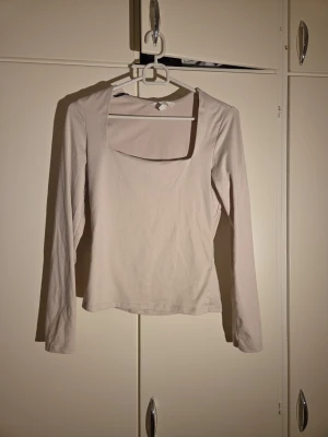 Beige långärmad topp från H&M - Säljer en beige långärmad topp från H&M i storlek S. Toppen har en fyrkantig halsringning och är tillverkad av mjuk polyester med elastan för stretch. Enkel och stilren design som är lätt att matcha med olika outfits.