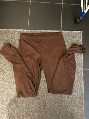 Bruna ribbade leggings/yoga pants - Säljer ett par bruna leggings med ribbad struktur. De har en enkel design med elastisk midja och är gjorda i ett mjukt och stretchigt material som sitter skönt mot kroppen. Perfekta för en chill och avslappnad stil.