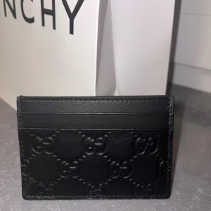 Äkta Svart kortfodral från Gucci i skinn - Säljer ett stilrent svart kortfodral från Gucci med präglade GG-loggor över hela framsidan. Fodralet har flera fack för kort och är tillverkat i mjukt skinn. Perfekt för dig som vill ha en lyxig och smidig accessoar i fickan.