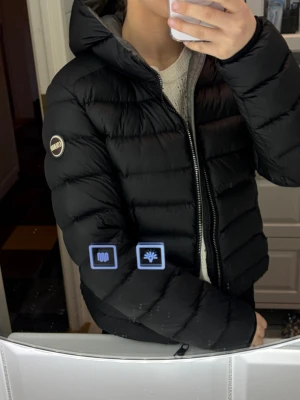 Svart Colmar dunjacka med huva - Säljer en svart dunjacka från Colmar med huva och snygg quiltad design. Jackan har lång ärm, dragkedja framtill och en clean look som funkar till allt. Perfekt för dig som vill ha en varm och stilren jacka under vintern. Det är en varm jacka i fint skick, men täcken på användning. Nypris ca 5000kr, äkta självklart