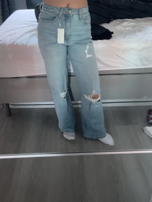 Ljusblå ripped wide jeans - Säljer ett par ljusblå jeans med breda ben och snygga slitningar på båda knäna. Byxorna har hög midja och klassisk femficksdesign. Materialet är jeans och passformen är loose med en modern wide stil. Perfekt för dig som gillar en avslappnad look. Säljer då jag fick i julklapp men är för små för mig. Nypris 500