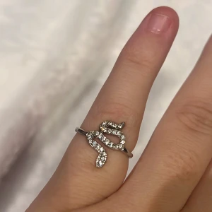 Orm ring från guldfynd - En silverfärgad ring med en orm på framsidan. Ormen har små kristaller på sig. Den saknar 1 kristal och som ni kan se på bilderna så är den lite ihop klämd, men det går att fixa. Jag vet tyvärr inte vilken storlek den är i. Nypris 229kr 