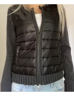 Svart och grå pufferjacka  - SÅ SNYGG CARDIGAN har i storlek 36,38 och 40❤️ på bilden är de storlek 36! Snygg pufferjacka i svart med grå stickade ärmar och ribbad kant. Jackan har dragkedja framtill och två fickor. Kroppsdelen är quiltad och ger en cool kontrast Snygg pufferjacka frånmed svart quiltad framsida och grå stickade ärmar. Jackan har dragkedja framtill, ribbad kant vid midjan och två fickor. Perfekt för dig som vill ha en cool och bekväm look under hösten och vintern.