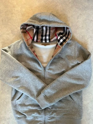 Burberry zip hoodie grå - Jätte fin, mått finns bra skick. Tog bort snöre= tycker det är snyggare. Men kan skicka med snöre om man vill. Armhåla till armhåla =50 cm.   Ärmarna= 57 cm Längd=61 cm