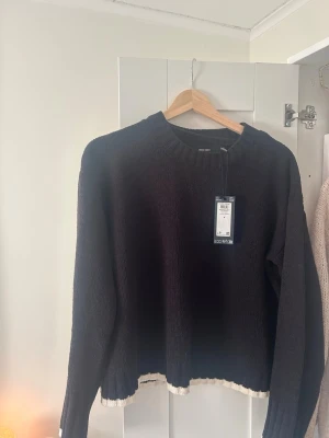 Svart stickad tröja med vit kant  - Svart stickad tröja med krämvita kanter från Vero Moda .Helt oanvänd med lappen kvar.Säljer då den är lite liten i passformen för min smak.Storlek M men liten i storleken 