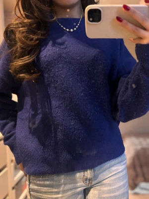 Blå stickad tröja med lång ärm - Mysig blå stickad tröja med rund hals och långa ärmar. Tröjan har en loose passform och är perfekt att matcha med jeans. Materialet känns mjukt och fluffigt, vilket gör den extra skön att bära under kyliga dagar.