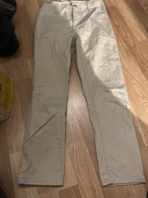 Beiga chinos med raka ben - Snygga beiga chinos med klassisk rak passform och knappgylf. Byxorna har bälteshällor och är gjorda i ett mjukt bomullsmaterial som känns skönt mot huden. Perfekta för dig som gillar en clean och enkel stil. Passar till sneakers eller boots.