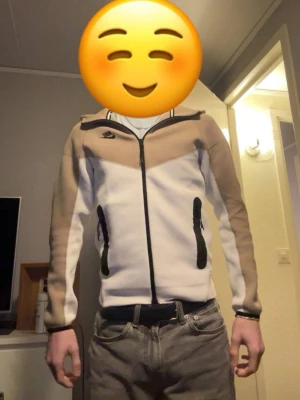 Nike beige och vit Nike tech - Nike tech i beige och vitt med svarta detaljer. Tröjan har hel dragkedja framtill, två svarta dragkedjefickor och en sportig look. Perfekt för dig som gillar stilrena och bekväma plagg. Nike-logga på bröstet och xs passform. Passar S och M