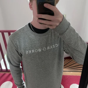 Grå sweatshirt från Ocean Works - Säljer en stilren grå sweatshirt från Ocean Works med vit logga framtill. Tröjan har rund halsringning, långa ärmar och är tillverkad i mjuk bomullsblandning. Perfekt för chill dagar eller när du vill ha en clean look. Storlek M och passar true to size. Bara höra av dig om du har några frågor. Priset går att diskuteras vid snabb affär