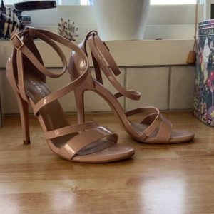 Beiga lackade klack-sandaler - Snygga beiga sandaler med hög klack från Anna Field. Skorna har flera smala remmar i glansigt lackmaterial och en justerbar rem runt vristen med guldfärgat spänne. Öppen tå och stilren design som lyfter varje outfit.