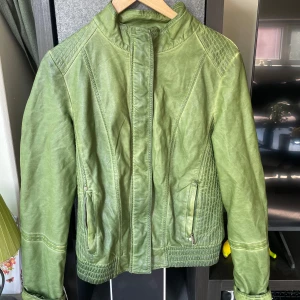 Y2k skinnjacka från BluDeise Fashion XL - Snygg grön skinnjacka från BluDeise Fashion i storlek XL. Jackan har coola quiltade detaljer på axlar och rygg, dragkedjor vid fickorna och en hög krage. Perfekt för dig som vill sticka ut med en unik färg och stilren look.
